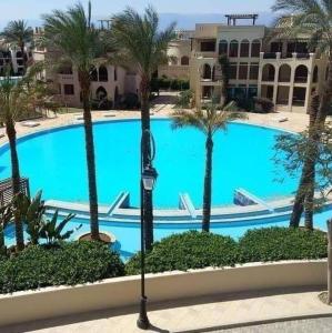 een groot zwembad met palmbomen voor een gebouw bij Lovely first floor tow bed rooms overviewing circular pool in Talabay Aqaba in Aqaba