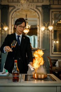 Um homem de fato está a agitar um caldeirão com fogo. em ホテル長楽館 京都 祇園 em Quioto