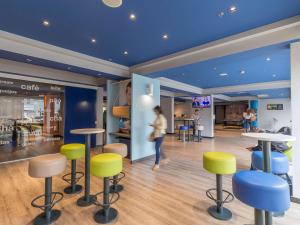 a woman walking through a room with stools and tables at ibis budget Curitiba Centro in Curitiba