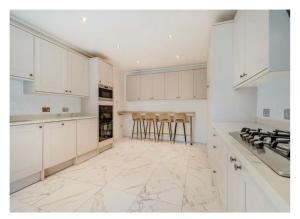 a white kitchen with white cabinets and bar stools at 8 bedroom Annexe at Moulton Grange in Northampton