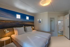 a bedroom with a large white bed and a bathroom at Strandhotel Noordzee in De Koog