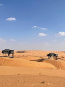 dwie ławki siedzące na piaskowej pustyni w obiekcie Moon Light Camp w mieście Badīyah