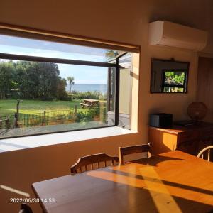 een eetkamer met een groot raam met uitzicht op een tuin bij Beachfront Bliss - Your Parapara Seaside Retreat in Parapara 