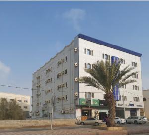 a large white building with a palm tree in front of it at اجنحة ارمادا in Al Qunfudhah