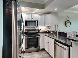 Una cocina con gabinetes blancos y un refrigerador de acero inoxidable. en Crystal Shores #1302, en Gulf Shores