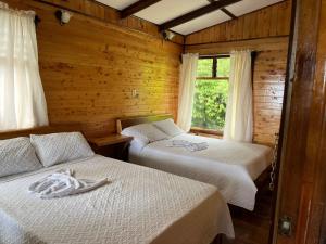 Habitación de madera con 2 camas y ventana en Cabañas el Bosque, en Turrialba