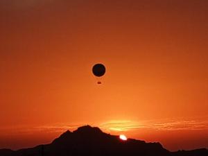 een heteluchtballon die bij zonsondergang over een berg vliegt bij Petra Rose Apartment in Wadi Musa