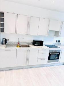 una cocina blanca con armarios blancos y fregadero en Ace Apartments, en Barking