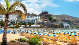 una spiaggia con molte sedie e ombrelloni di MGT - Appartamento sulla Spiaggia con terrazza romantica a Puerto Rico de Gran Canaria