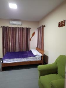 a bedroom with a bed and a green chair at Sa-Ra's vakantiehuis in Paramaribo