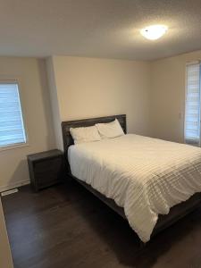 a bedroom with a bed with a white comforter and two windows at ON Residence in Hamilton