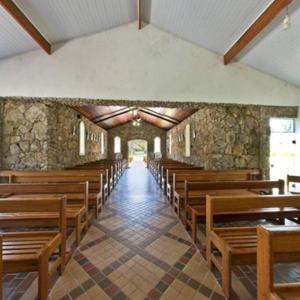 um corredor de igreja com bancos de madeira e uma parede de pedra em Morada dos pássaros Boracéia em Bertioga