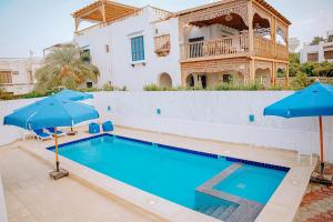 a swimming pool with blue umbrellas in front of a house at 4 bedrooms villa with private pool in Tunis village faiuym in Qaryat at Ta‘mīr as Siyāḩīyah