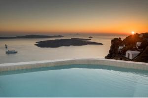 a swimming pool with a sunset in the background at Aqua Luxury Suites Santorini in Imerovigli
