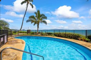 a swimming pool with palm trees and the ocean in the background at Hale Hui Kai in Wailea