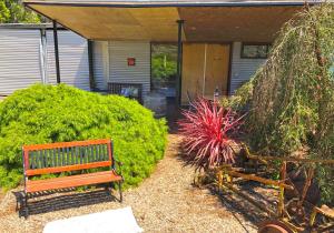 a wooden bench sitting in a yard next to some bushes at Valley Farm Vineyard Villas in Healesville