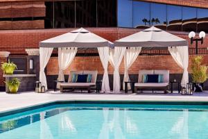 uma piscina com dois guarda-sóis e cadeiras ao lado de um edifício em Scottsdale Marriott Old Town em Scottsdale