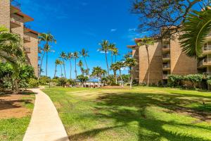 a walkway in front of a building with palm trees at Kauhale Makai 122 in Kihei