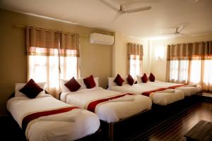 a group of four beds in a room with windows at Hotel Vista Chitwan in Sauraha