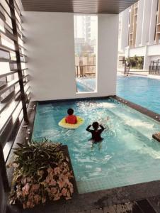 two people in a swimming pool with a surfboard at Sky Tree Studio Apartment at Bukit Indah, Johor in Johor Bahru