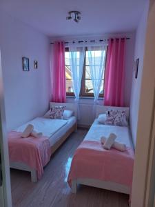 two beds in a room with pink curtains and a window at Apartament Paryski in Karpacz