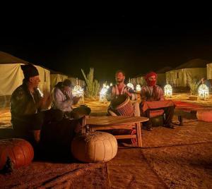 a group of people sitting around a table in front of tents at Sahara wild camping in Mhamid