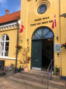 żółty budynek z zielonymi drzwiami i dwoma flagami w obiekcie Cafebrumman w Nexø
