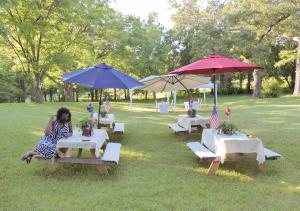 una mujer sentada en mesas de picnic bajo sombrillas en RusticParaiso: Family, Team & Group Urban Retreat en Greensboro