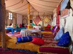 ein Zimmer mit vielen Kissen und Tischen in einem Zelt in der Unterkunft Authentique berber Camp in M’hamid El Ghizlane