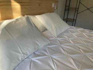 1 cama no hecha con sábanas y almohadas blancas en Apartamentos Los Pocillos, en Gargantilla del Lozoya