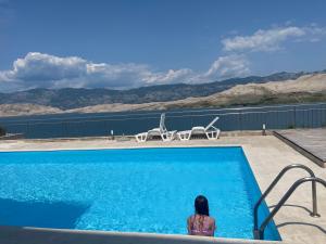 a woman sitting next to a swimming pool at Studio Apartment Pag Luxury 4U in Pag