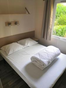 1 cama blanca con 2 almohadas y ventana en Mobil-Home 6 personnes avec clim N' B025, en Boofzheim