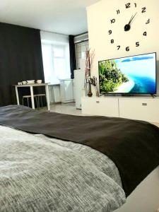 a bedroom with a large bed with a clock and a tv at Уютная студия на Ауэзова 3 in Ustʼ-Kamenogorsk