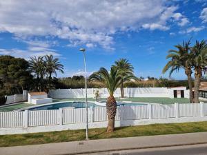 uma palmeira ao lado de uma cerca branca com uma piscina em Laguna79 Vacaciones Vera Playa em Vera