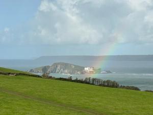 a rainbow over the ocean with a house on a hill at Bantham Beach Pad in Thurlestone