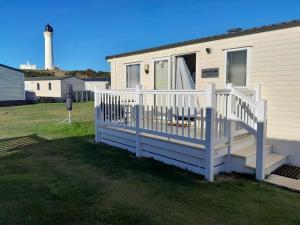 uma casa móvel com uma cerca branca e um farol em hollies retreat em Lossiemouth