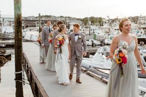 una sposa e uno sposo che camminano lungo un molo con la loro festa di nozze di The Hotel at Cape Ann Marina a Gloucester