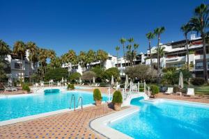 a large swimming pool with palm trees and buildings at Stunning Duplex Apartment in Puente Romano Resort in Marbella