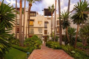 a large white building with palm trees and a walkway at Stunning Duplex Apartment in Puente Romano Resort in Marbella