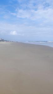 an empty beach with people walking on the sand at Sobrado com 3 quartos piscina 100m mar em matinhos in Matinhos
