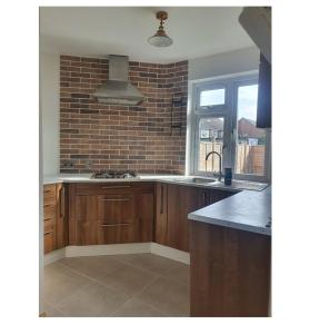 a kitchen with wooden cabinets and a brick wall at Ritzs place in Northolt