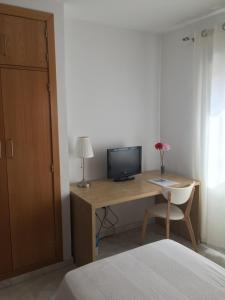 1 dormitorio con escritorio, TV y cama en Hostal Monteluna, en Rociana