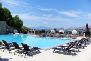 Ramada Resort by Wyndham Bodrum في بيتيس: حمام سباحة مع كراسي للاستلقاء ومجموعة من التجهيزات