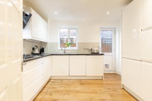 a kitchen with white cabinets and a wooden floor at 5 Bed House Heathrow Egham Virginia Water Sleeps 7 or 8 sharing in Egham