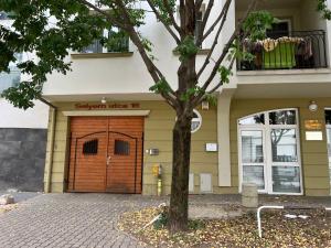 a tree in front of a building with a wooden garage at City Lux Apartman in Nyíregyháza