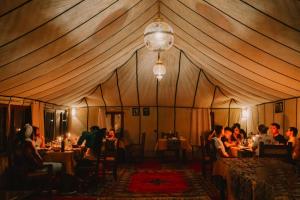 a group of people sitting at tables in a tent at desert camp in Hassilabied