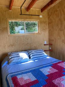 uma cama num pequeno quarto com uma janela em Cabaña de campo con vista al mar em Ancud