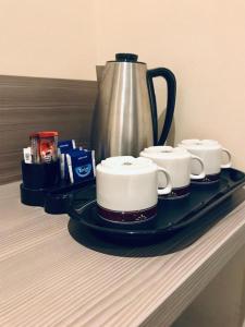 a tray with three coffee cups and a kettle on a counter at Qotel Hotel Ashok Vihar Couple Friendly in New Delhi