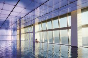 uma mulher sentada numa piscina num edifício com janelas em The Ritz-Carlton Hong Kong em Hong Kong