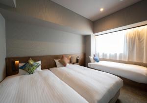 two beds in a room with a window at Hotel Oriental Express Fukuoka Nakasu Kawabata in Fukuoka